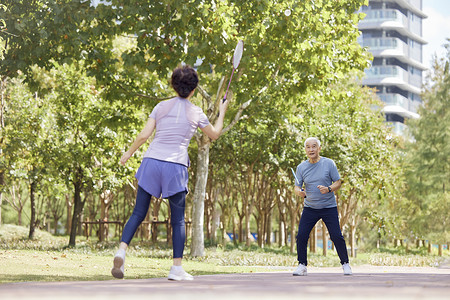 男孩在打网球在公园打羽毛球的老年夫妇背景