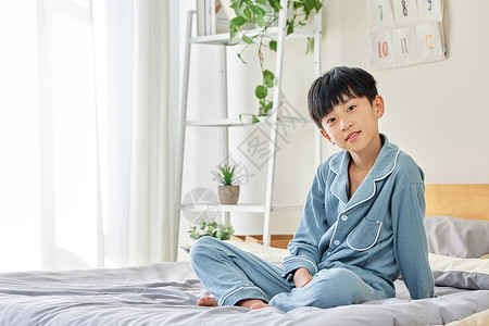 穿睡衣坐在床上的小男孩背景图片