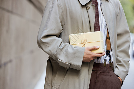 穿风衣的都市男性手拿礼物盒特写背景图片