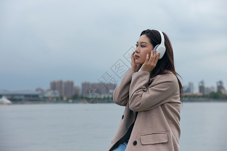 在江边带着耳机伤感情绪的年轻女性背景