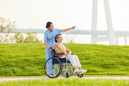 年轻女护工户外照顾轮椅老人背景图片