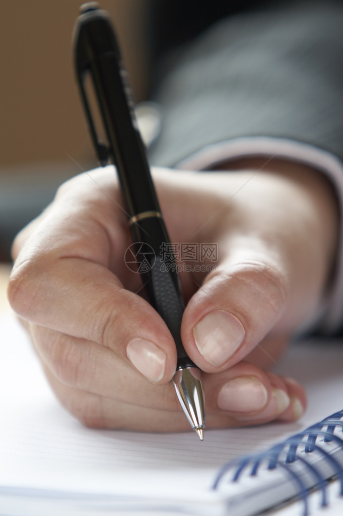 女商人手拿笔在记本上写字的特写图片