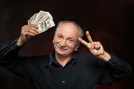 幸运的老人拿着一帮美元钞票和手指在图片