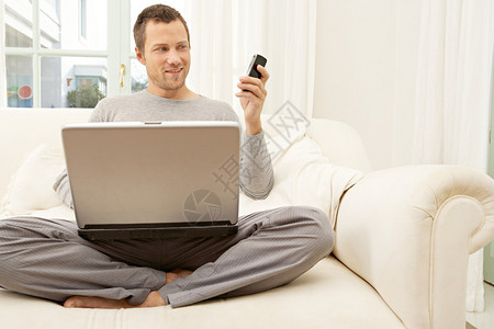 专业青年男子在家里坐在白色沙发上时使用笔记本电图片