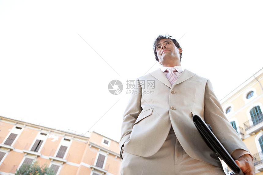 一个年轻的商人站在一个经典的办公大楼广场与他身后的天空与工作文图片