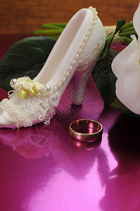 粉红色背景的白玫瑰新娘花束与幸运鞋和结婚戒指图片
