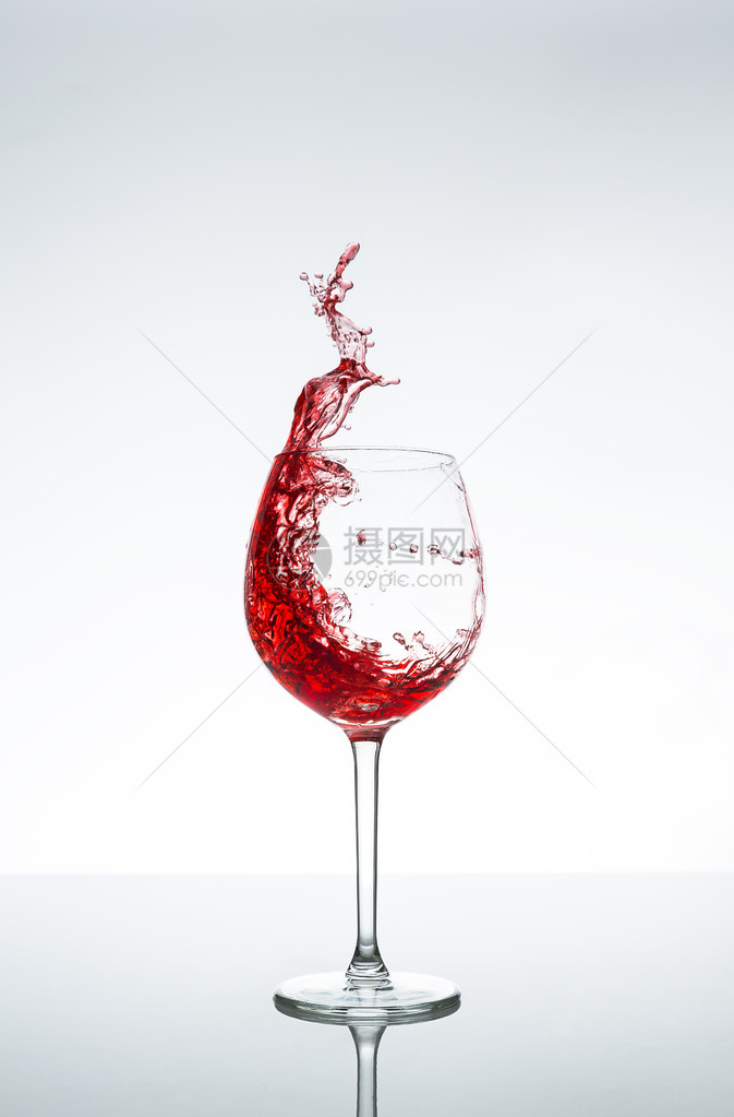 红酒杯和红酒喷洒在白色灰背景上图片