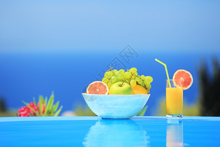 一杯橙汁和一碗不同水果旁图片