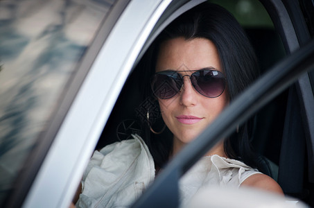 戴太阳镜的时尚年轻女士驾驶汽车从开着的窗户外看镜头图片