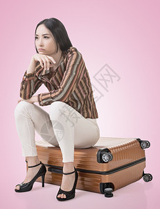 亚洲女人坐在行李上思考背景图片