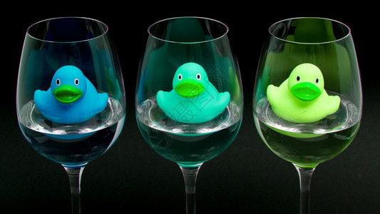 酒杯中的蓝色和绿色橡胶鸭深色背景图片