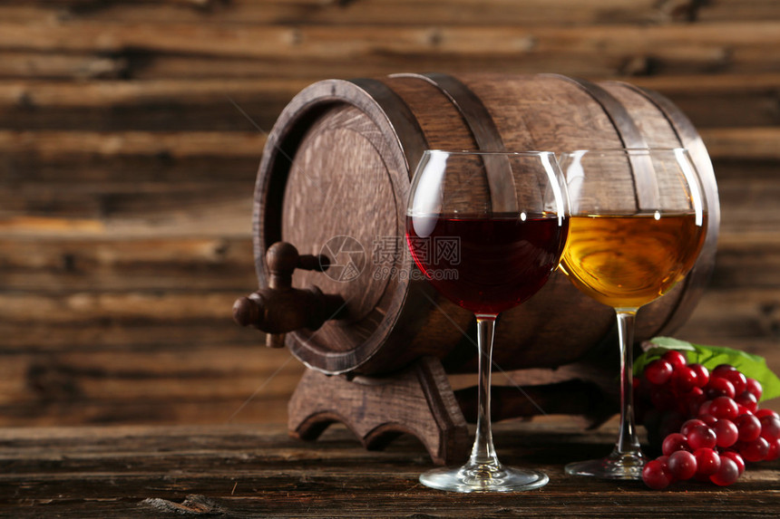 棕色木质背景上的红白葡萄酒杯和酒桶图片