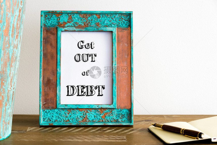 在白墙背景的木制桌边壁上挂着带有激励信息摆脱债务图片