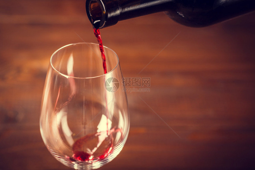 在木质背景下将红酒倒入玻璃杯中图片