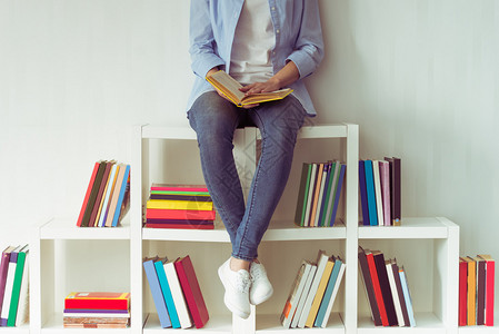 穿牛仔裤的漂亮女孩拿着一本书坐在书图片