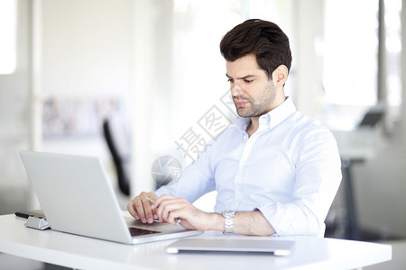 在办公室工作时坐在膝上型电脑桌上的一位英俊的文艺主背景图片