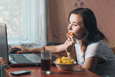 女人用芯片在笔记本电脑上吃薯片家里的黑发女郎看电影图片