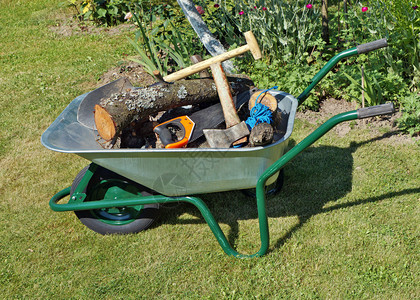 铲子锯子绳子和树桩都放在一辆绿色的手动单轮独车里独轮车在花园草坪上阳图片