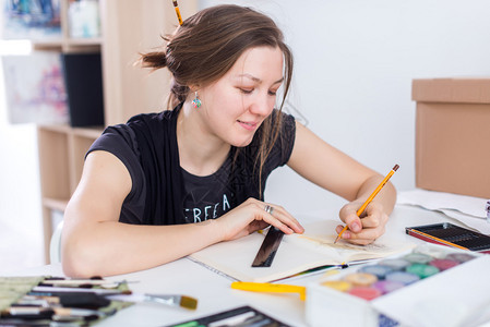 年轻的女艺术家在工作室的工作场所使用素描本用铅笔绘制素描受启发的画家图片