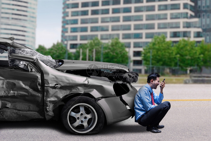 交通事故后坐在破车前用手机说话的愤怒男人图片