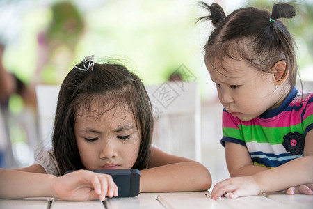 两个小亚洲女孩坐在椅子上用手机在公园户图片