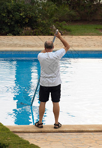 男子用杆清洗游泳池图片
