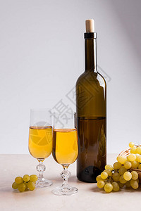 两杯白葡萄酒和浅色大理石背景上的棕色瓶白葡萄酒眼镜附近黄色木篮里图片