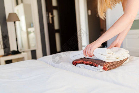 年轻酒店女佣把新鲜毛巾放在床上图片