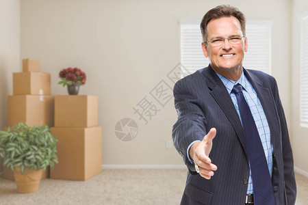 微笑的商人伸手在空荡的房间里与包装盒握手图片