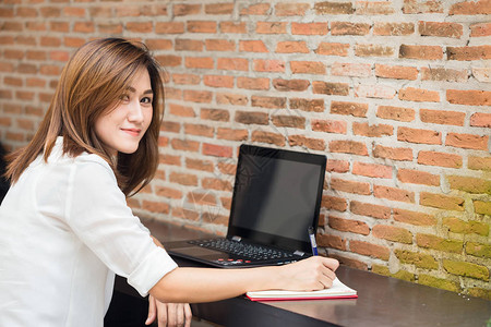微笑思考做工作的职业女商务工作家认为并在笔记本或电脑笔记图片