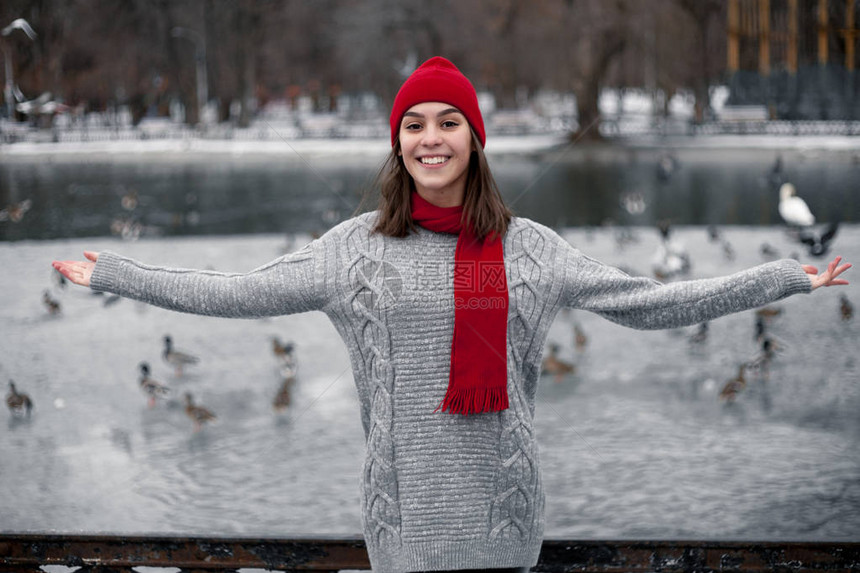 穿着红帽子和围巾的女孩在湖边的冬季公园散步图片