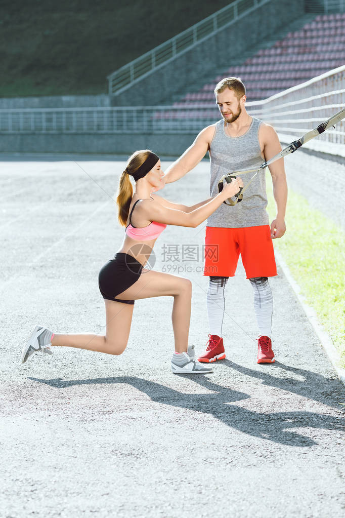 穿着玫瑰顶和黑短裤的运动女运动员在体育场上通过训练环进行操练图片