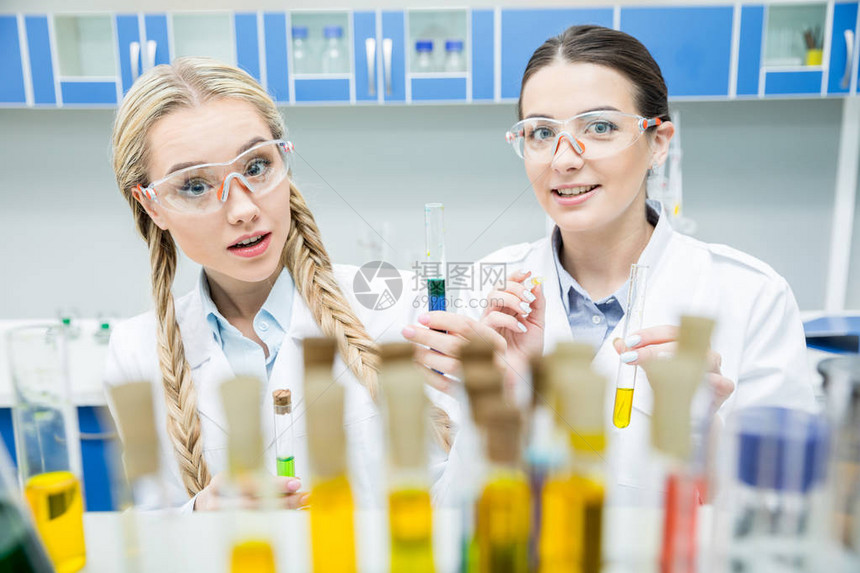 实验室大衣中的年轻女科学家在化学实验室中共图片