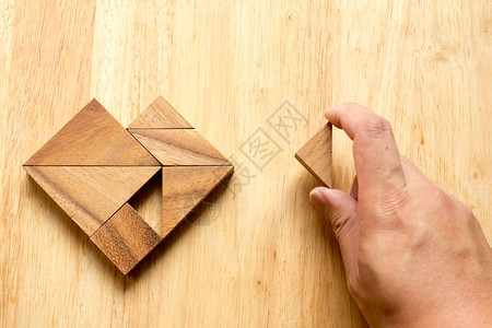 人类握着一张图文拼图来完成木桌上的心脏形状背景图片
