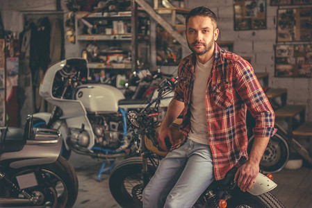 穿便衣的帅哥在修理店坐在摩托车上时正在看照相机图片