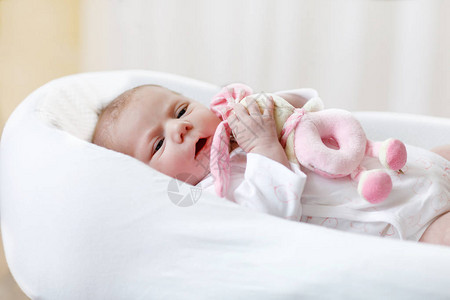 可爱的新生婴儿玩粉红色毛绒动物拨浪鼓玩具在家里的白色床上新出生的孩子图片