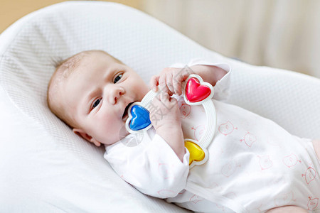 可爱的新生婴儿玩五颜六色的拨浪鼓玩具在家里的白色床上新出生的孩子图片