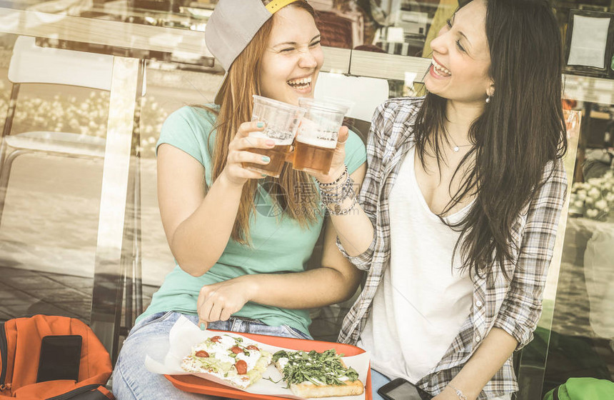 年轻女在户外酒吧餐厅吃比萨饼和喝啤酒与快乐的女朋友一起度过快乐时光的友谊概念复古去饱和老式过滤器上图片