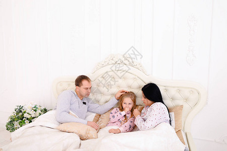 用纸巾擦鼻子孩子和爸妈在床上年轻夫妇照顾他们的女儿长黑发的女人背景图片