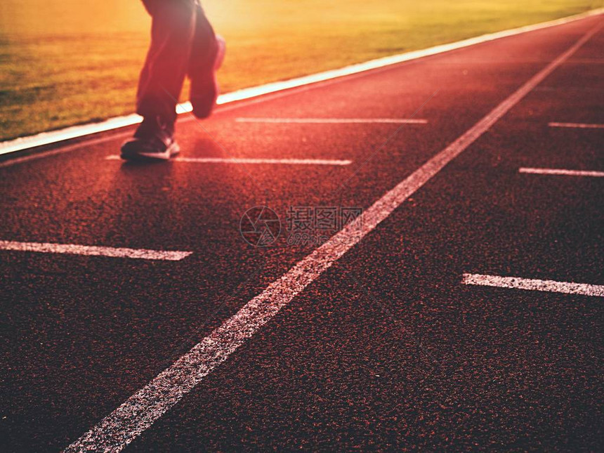 男子双腿穿着跑鞋在室外体育场的红色跑道上奔跑太阳光线和身体阴影体育和健康生活方式图片