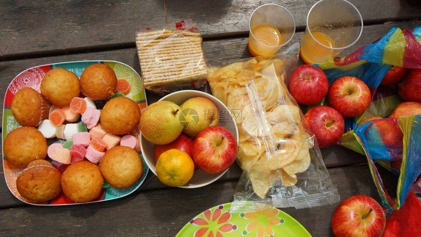 红苹果梨子橘子咸饼干含薯片的塑料袋和在生锈木制桌上的纸杯图片