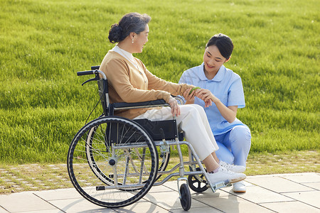 女护工在公园给坐轮椅的老人按摩康复图片