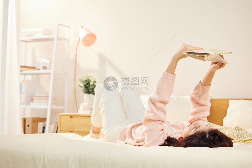 年轻美女卧室躺在床上看书图片