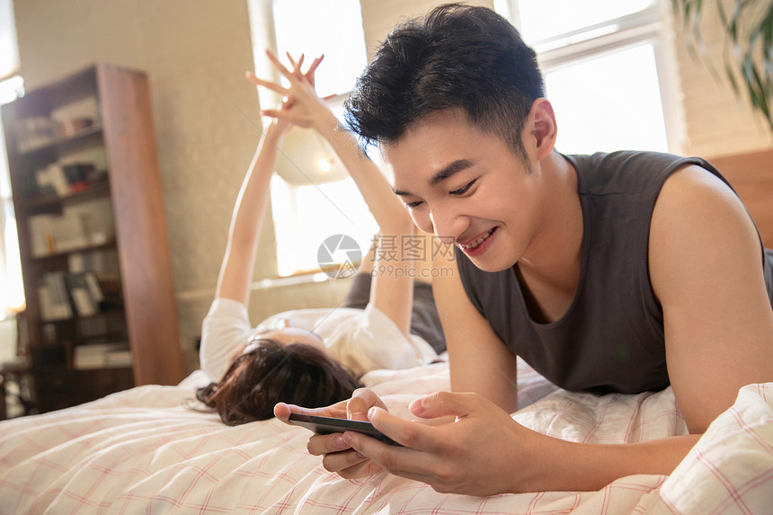 青年情侣趴在床上玩手机图片
