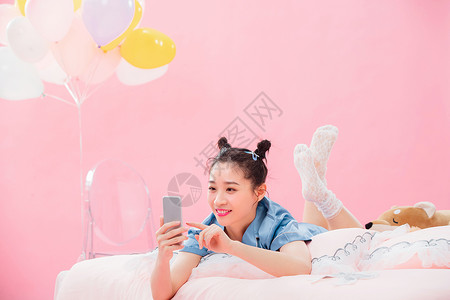 聊天气球年轻女孩趴着在床上使用手机背景