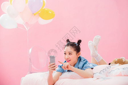 聊天气球年轻女孩趴着在床上使用手机背景