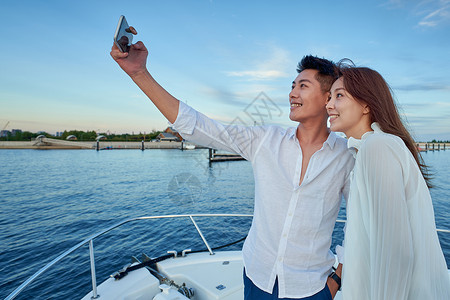 游艇上的人青年夫妇站在游艇上用手机拍照背景