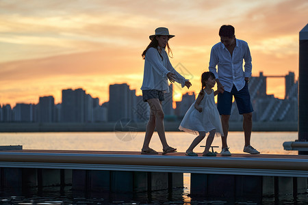 夕阳下放风筝剪影一家三口在海边玩耍背景