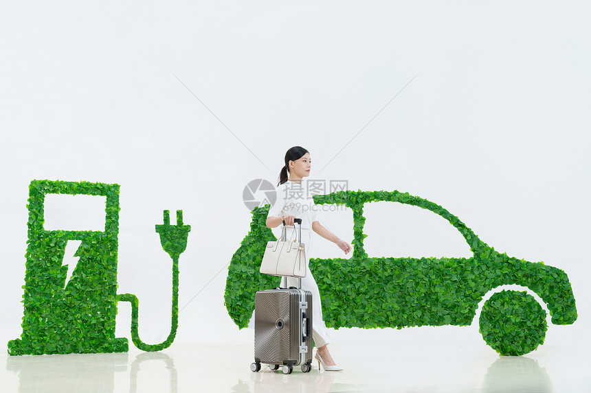 商务女士推着行李箱走在电动汽车旁图片