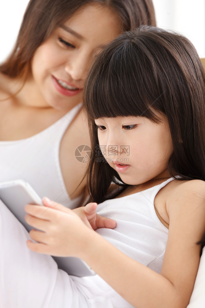 母亲和女儿在卧室的床上使用平板电脑图片